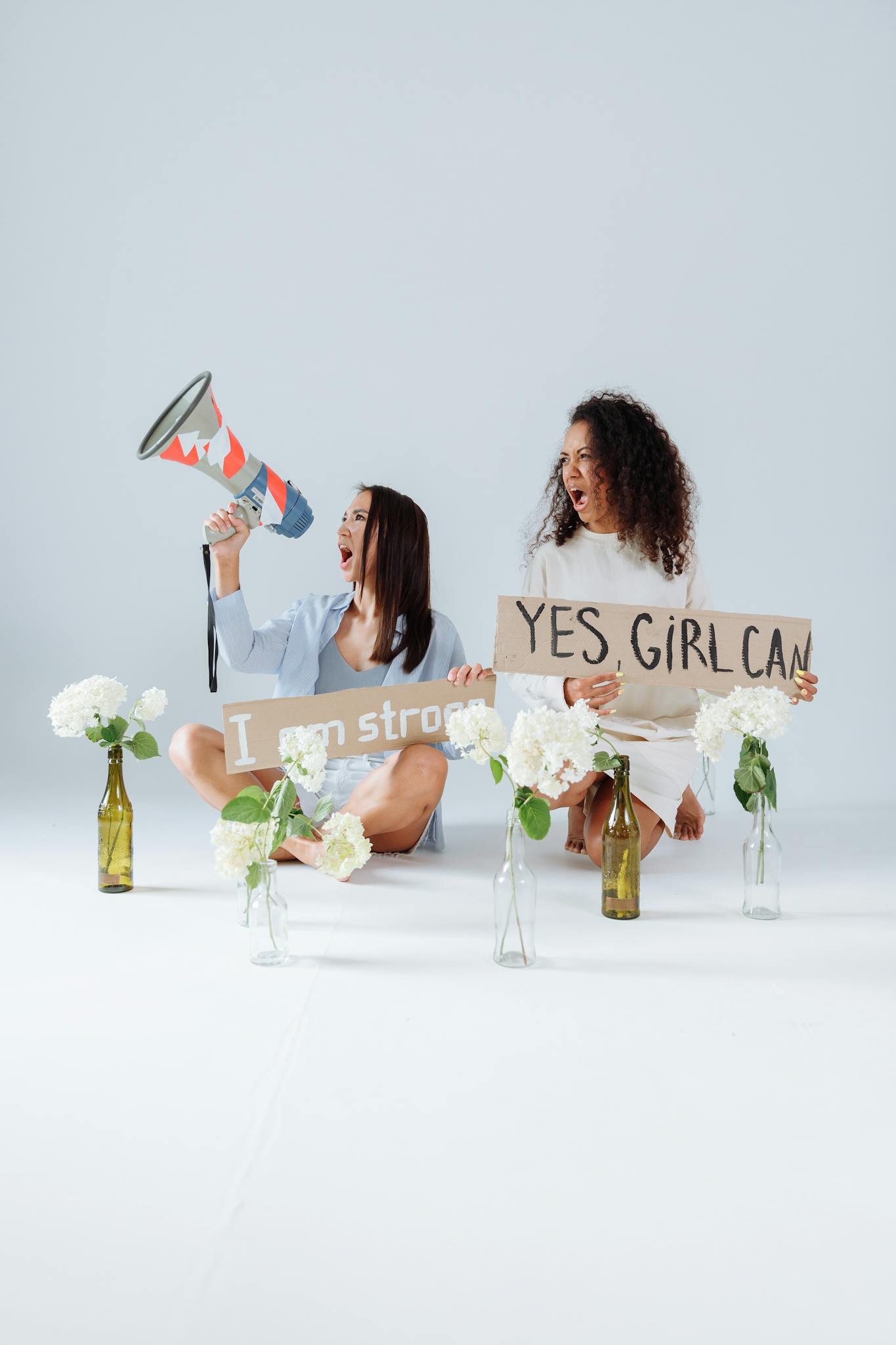 A diverse group of women holding empowering signs and megaphone for social activism in a neutral studio setting.